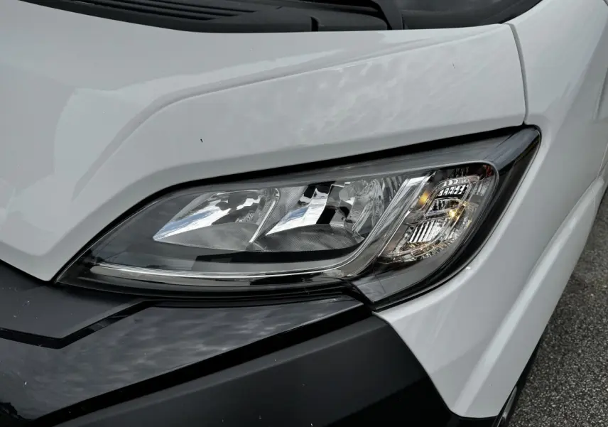 Gros plan sur le phare avant droit du Peugeot Boxer Fourgon blanc, soulignant les détails du bloc optique moderne.