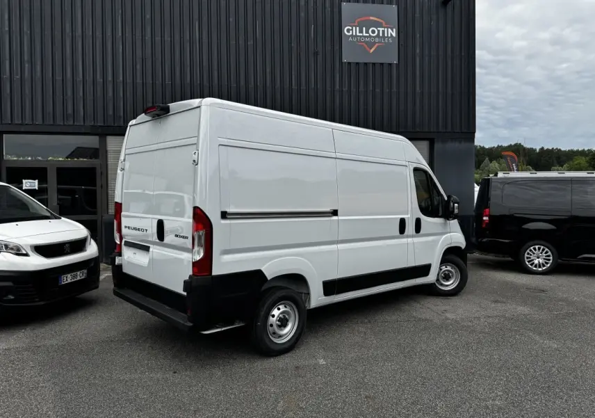 Vue 3/4 arrière droite d’un Peugeot Boxer Fourgon blanc stationné devant un bâtiment avec logo Gillotin Automobiles.