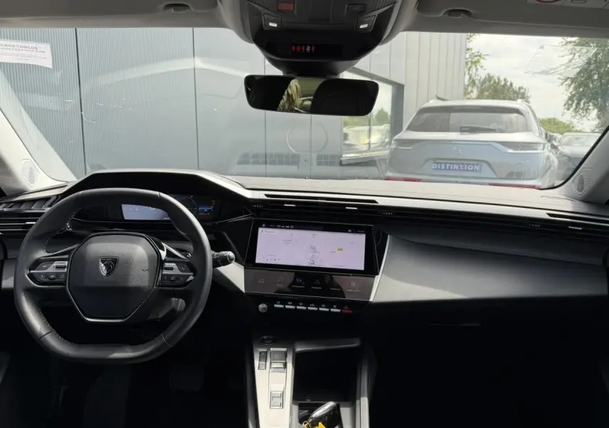 Vue intérieure avant du Peugeot 308 Hybrid 2025, tableau de bord noir avec écran tactile central et volant compact.