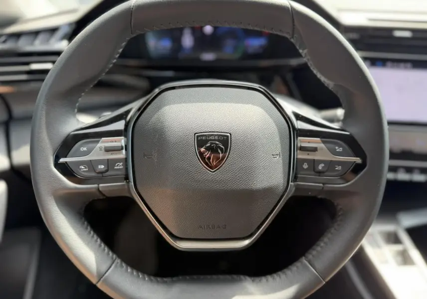 Vue rapprochée du volant cuir noir de la Peugeot 308 Hybrid 2025 avec commandes intégrées et logo central lion.