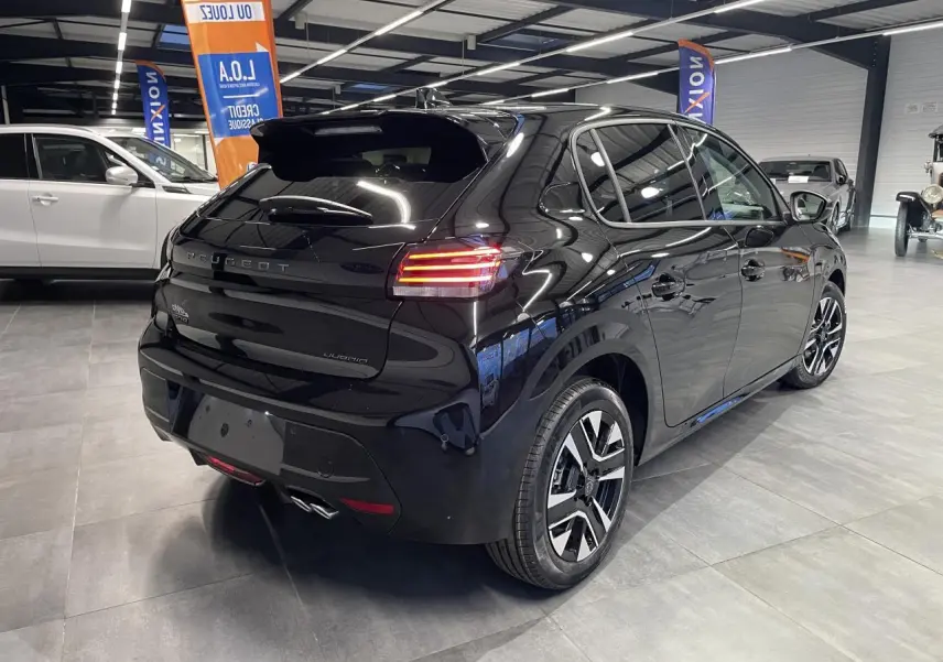 Peugeot 208 hybride noire métallisée vue 3/4 arrière droit en intérieur avec jantes alliage bi-tons et feux LED allumés.