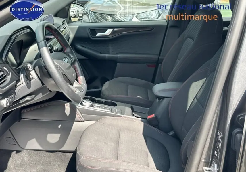 Vue intérieure côté conducteur du Ford Kuga gris foncé 2022, avec sièges sport et volant cuir à surpiqûres rouges.