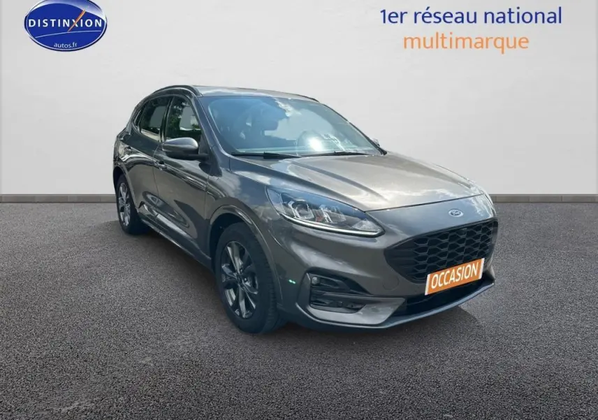 Ford Kuga gris foncé en 3/4 avant droit, avec jantes alliage 18 pouces et barres de toit visibles.