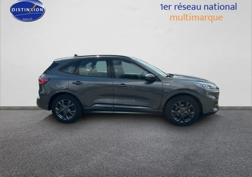Ford Kuga gris foncé vu de profil côté gauche, avec jantes alliage 18 pouces et barres de toit visibles.