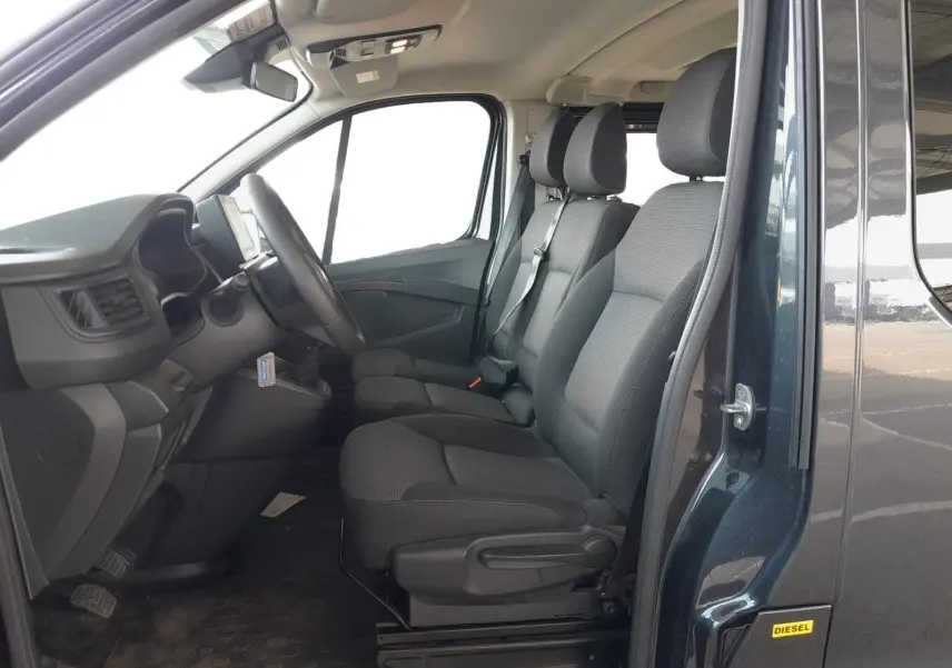 Vue intérieure côté conducteur du Renault Trafic Combi gris foncé, montrant les sièges avant et le tableau de bord.