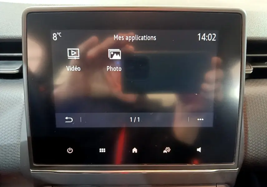 Écran tactile central affichant les applications vidéo et photo sur tableau de bord Renault Clio blanc, vue intérieure frontale.