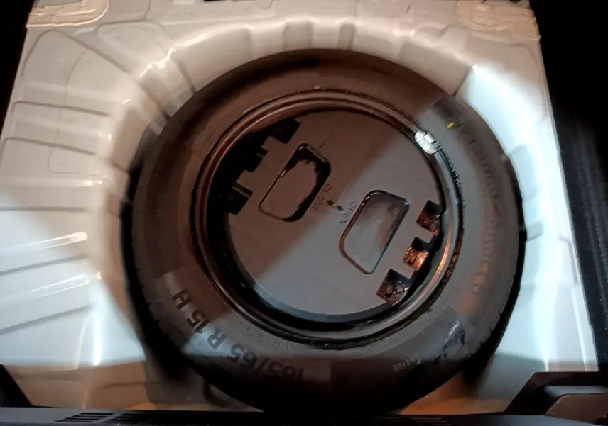 Roue de secours noire dans le coffre blanc d'une Renault Clio Business TCe 100 de 2019.