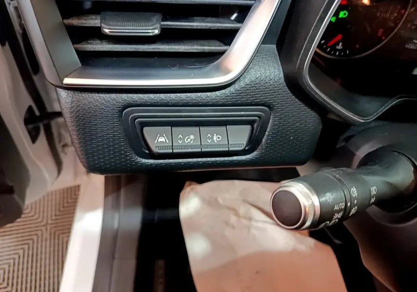 Gros plan sur les commandes d'assistance et réglages d'éclairage à gauche du volant d'une Renault Clio Business blanche de 2019.