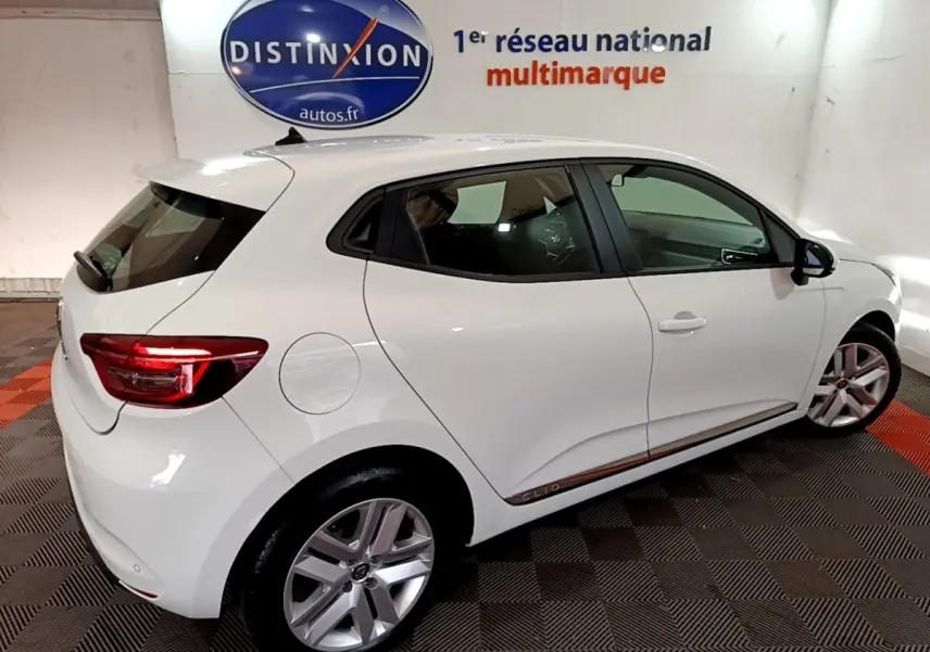Vue 3/4 arrière droite d'une Renault Clio Business blanche, avec jantes alliage et feux arrière LED allumés.