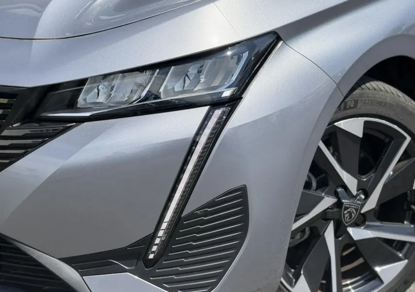 Gros plan sur l'avant droit gris Artense du Peugeot 308 Hybrid 145, mettant en valeur le phare LED et la jante alliage 17 pouces.