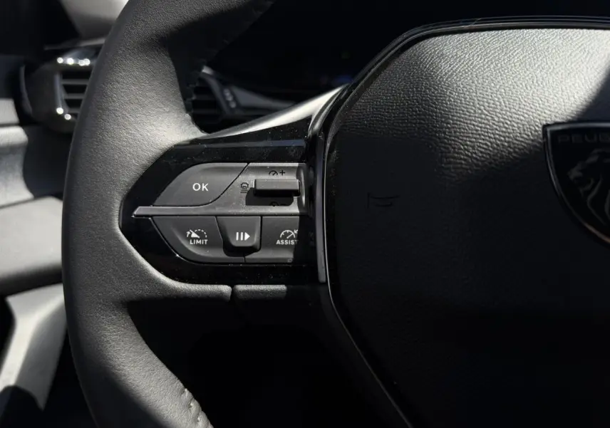 Gros plan sur le volant noir de la Peugeot 308 Hybrid 2025, avec commandes intégrées côté gauche et logo lion visible.