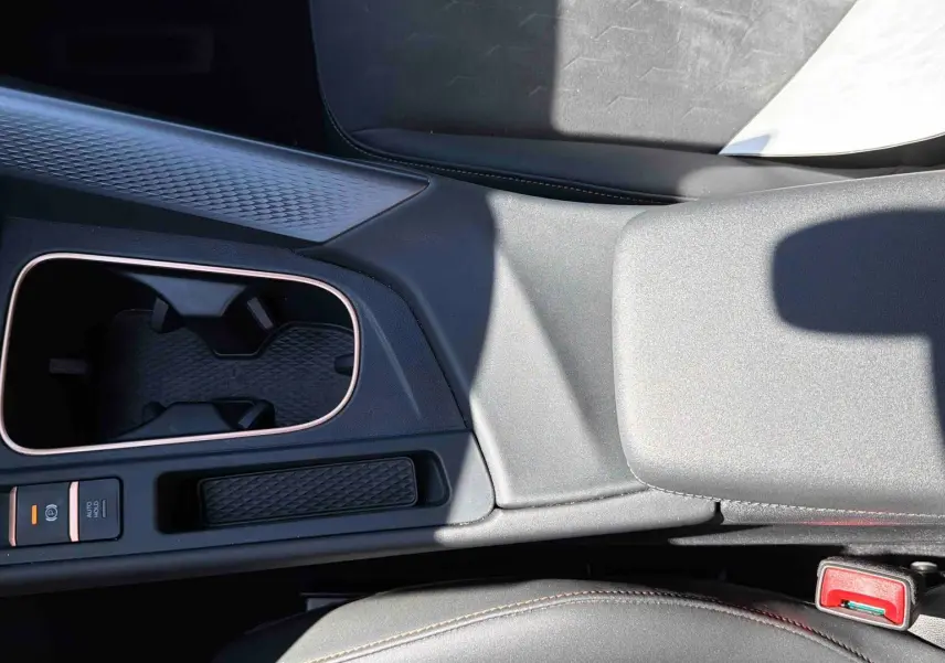Vue rapprochée de la console centrale grise du CUPRA TERRAMAR 1.5 eHybrid avec porte-gobelets et frein à main électrique.