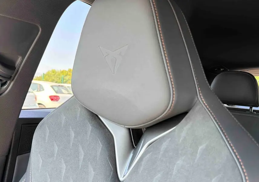 Gros plan sur l'appui-tête gris avec logo Cupra embossé, siège avant en cuir et tissu, intérieur du véhicule visible.