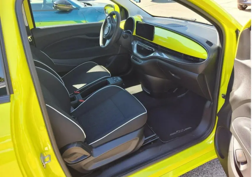 Intérieur de la FIAT 500 électrique jaune Acid vu côté conducteur, avec tableau de bord assorti et sièges noirs.