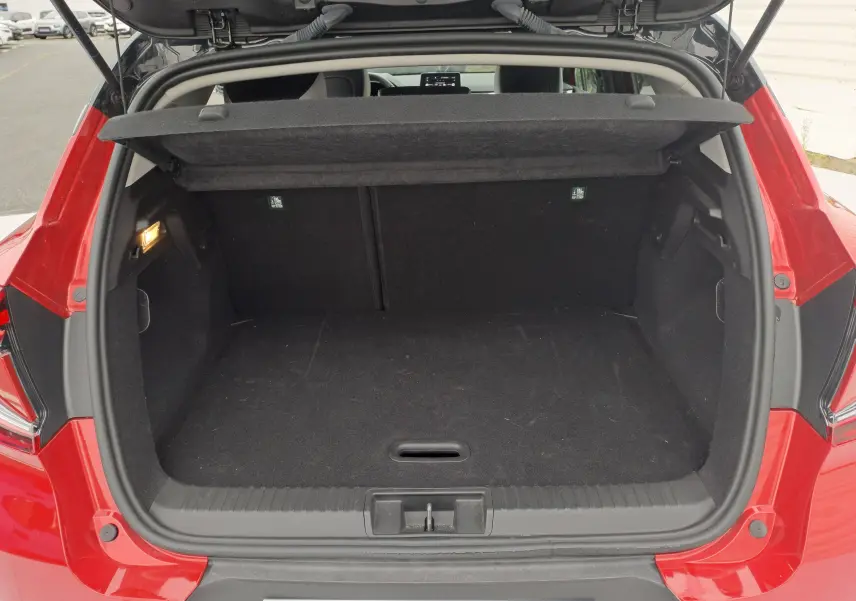 Coffre ouvert vu de l'arrière d'un Renault Captur 2024 rouge flamme métal, montrant un espace de chargement vide et propre.