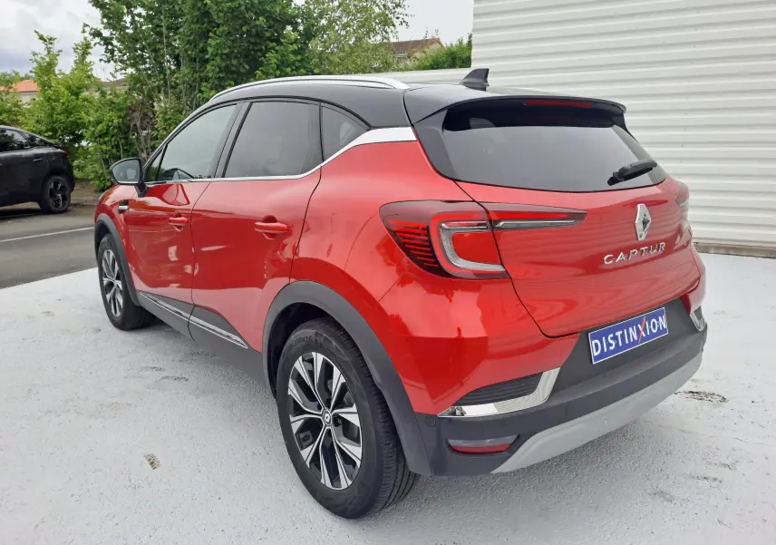Vue 3/4 arrière droite d'un Renault Captur 2024 rouge flamme métal avec toit noir et jantes alliage bicolores.