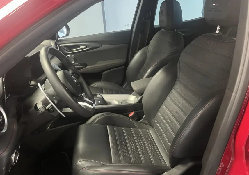 Intérieur côté conducteur de l'Alfa Romeo Tonale rouge 2024, sièges sport cuir noir avec surpiqûres rouges et volant sport.