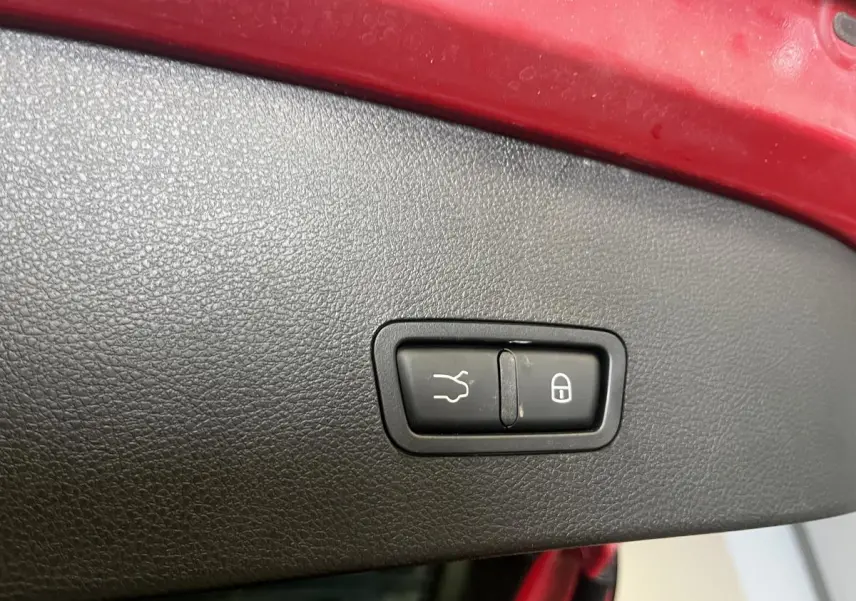 Gros plan sur le bouton de fermeture du coffre, entouré de plastique noir, sur un Alfa Romeo Tonale rouge.