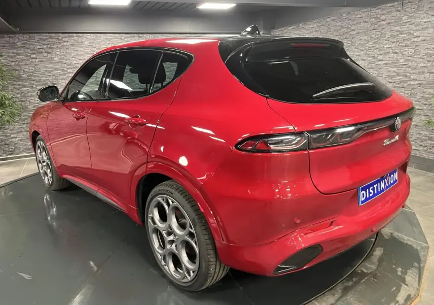 Vue 3/4 arrière droite de l'Alfa Romeo Tonale rouge avec jantes 20 pouces et toit noir en intérieur showroom.