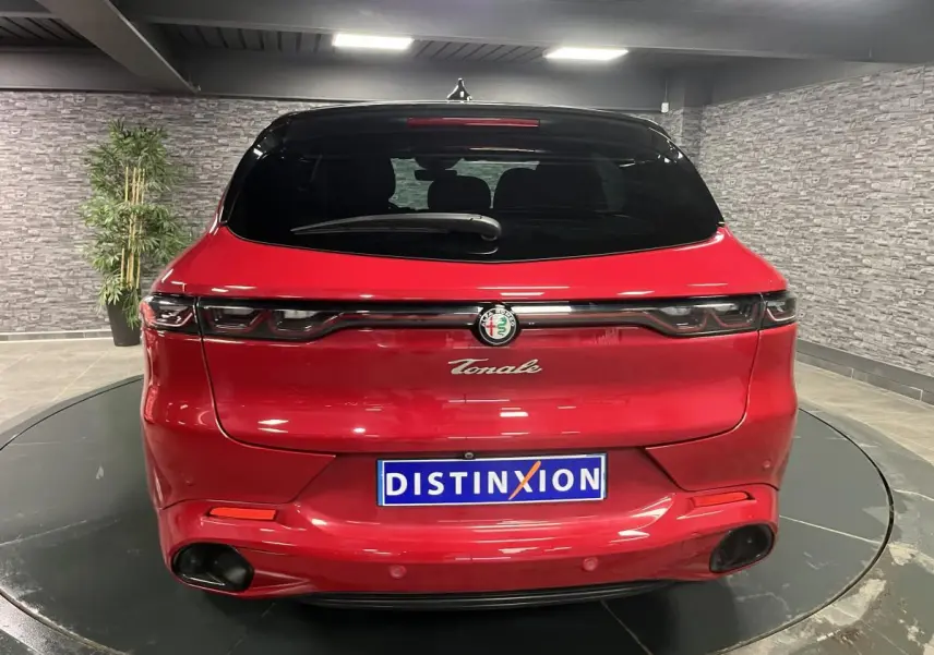 Vue arrière d'une Alfa Romeo Tonale rouge avec toit noir et feux arrière full LED dans un showroom.