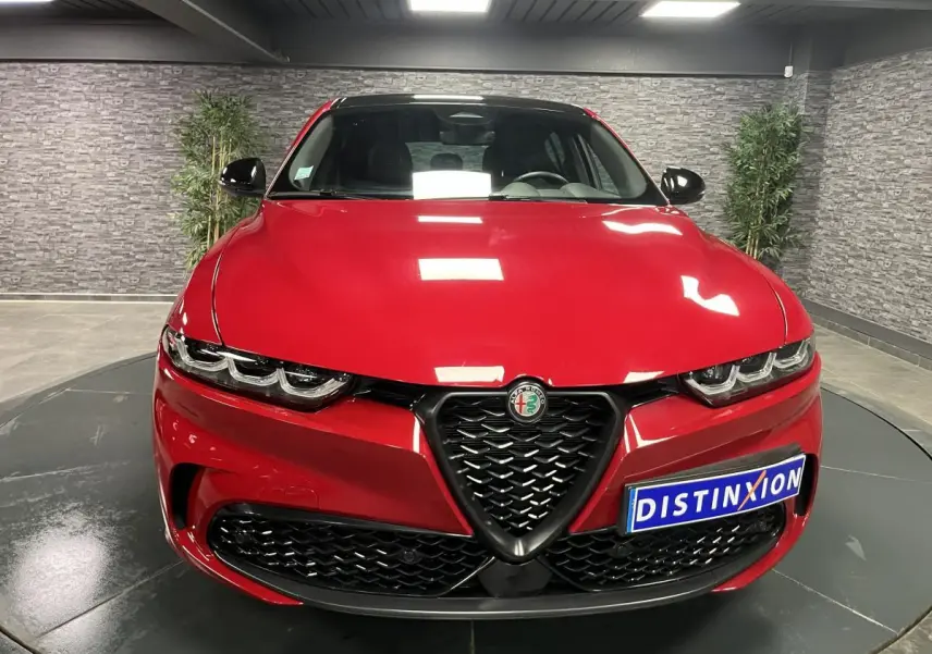 Vue frontale d'une Alfa Romeo Tonale rouge avec calandre noire et phares LED distinctifs dans un showroom.
