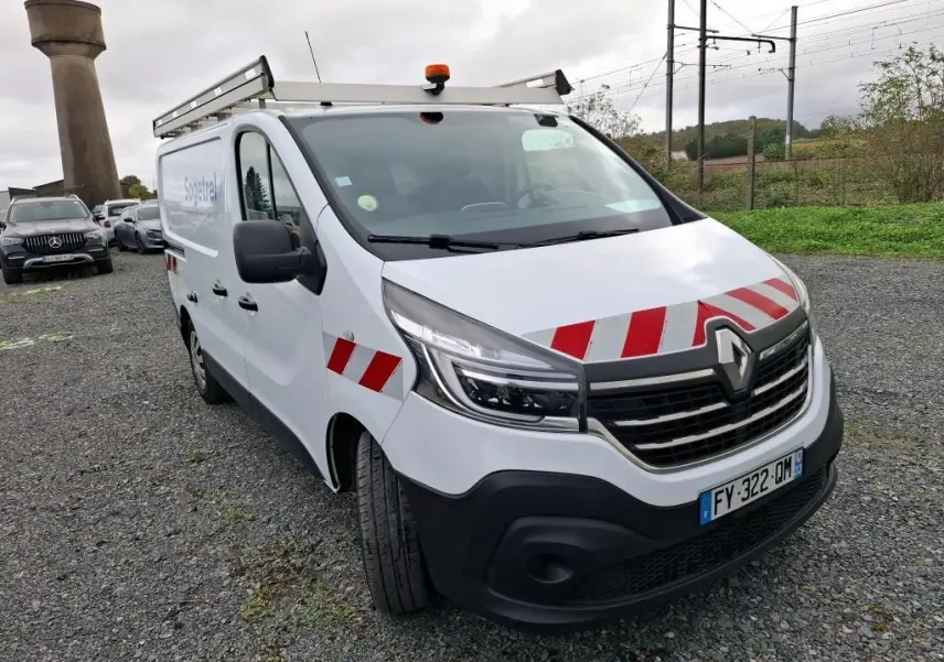 Renault Trafic Fourgon blanc en 3/4 avant droit avec bandes rouges réfléchissantes et galerie de toit.
