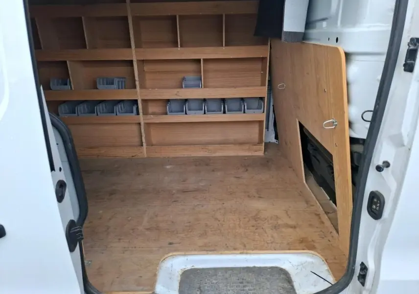 Vue intérieure arrière du Renault Trafic Fourgon blanc, montrant l'aménagement bois avec étagères et rangements intégrés.