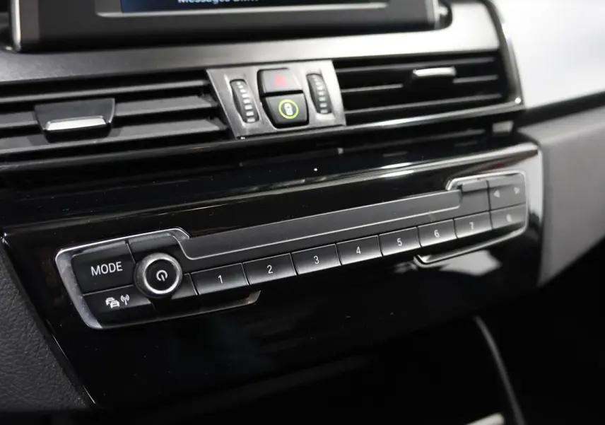 Gros plan sur la console centrale noire de la BMW Série 2 Active Tourer 216d, mettant en valeur les boutons de commande et l'écran supérieur.