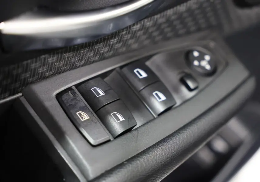Gros plan sur les commandes des vitres électriques côté conducteur d'une BMW Série 2 Active Tourer blanche, intérieur noir.