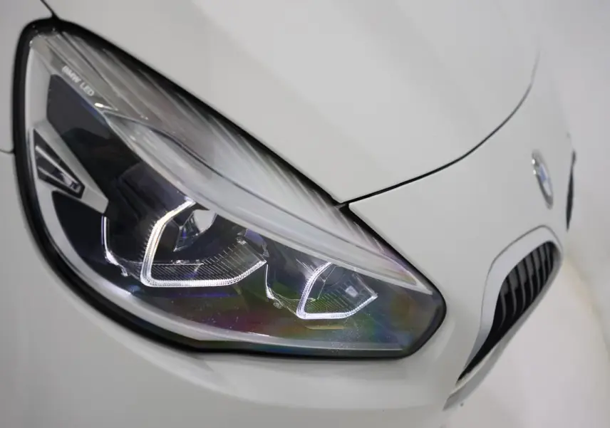 Gros plan sur le phare avant gauche blanc d'une BMW Série 2 Active Tourer 216d avec calandre caractéristique.
