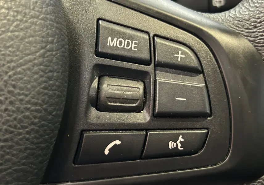 Gros plan sur les commandes noires du volant côté gauche de la BMW Série 2 Active Tourer blanche, boutons mode et téléphone.