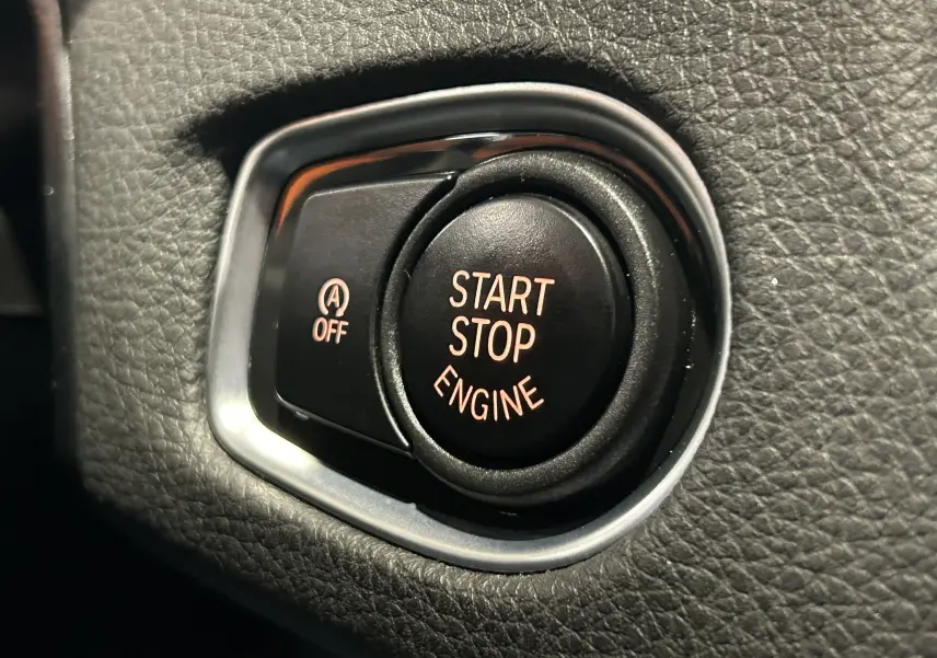 Gros plan sur le bouton noir Start Stop Engine entouré de cuir noir à l'intérieur d'une BMW Série 2 Active Tourer blanche.