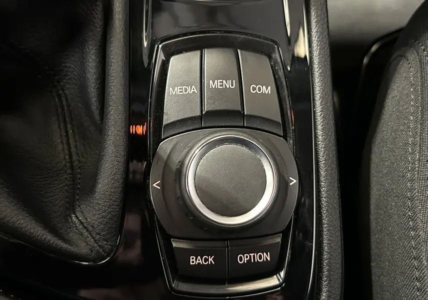 Gros plan sur la molette de commande centrale noire brillante de la BMW Série 2 Active Tourer blanche, entourée de boutons fonctionnels.