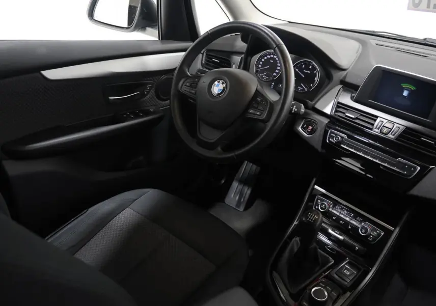 Vue intérieure côté conducteur de la BMW Série 2 Active Tourer blanche, avec volant cuir et boîte manuelle visible.