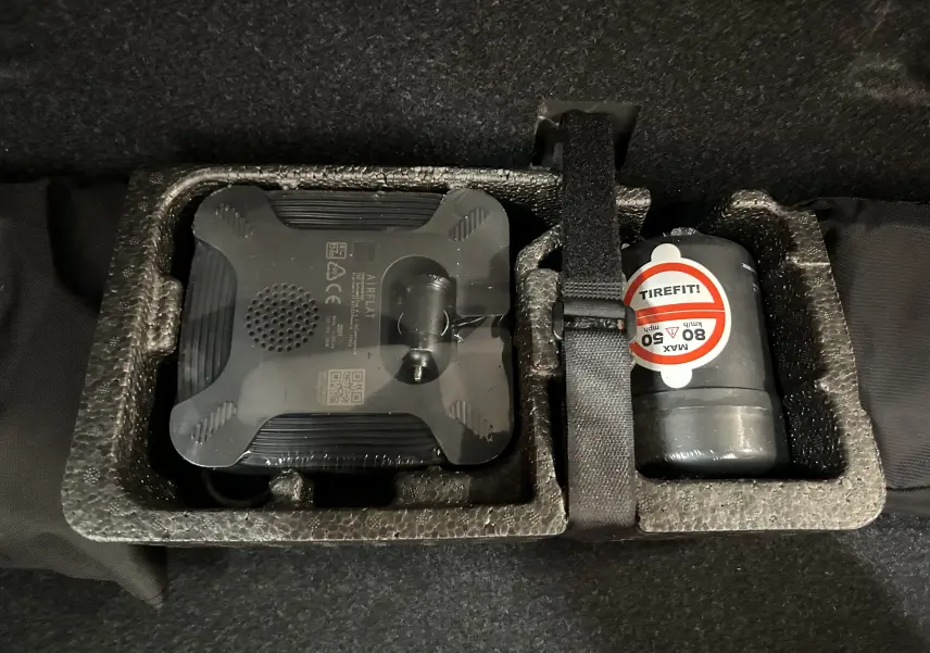 Gros plan sur le kit de réparation pneumatique noir et gris fixé dans le coffre d’une BMW Série 2 Active Tourer blanche.