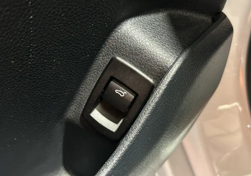 Gros plan sur le bouton d'ouverture du coffre noir dans l'habitacle d'une BMW Série 2 Active Tourer blanc.