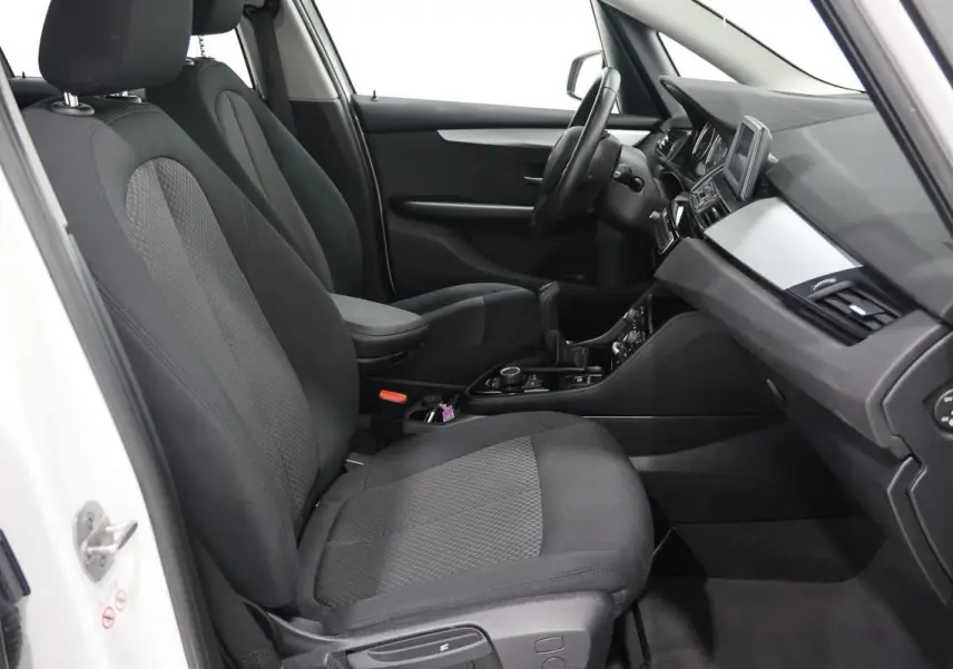 Vue intérieure côté conducteur de la BMW Série 2 Active Tourer blanche, sièges tissu noirs avec volant cuir et console centrale.
