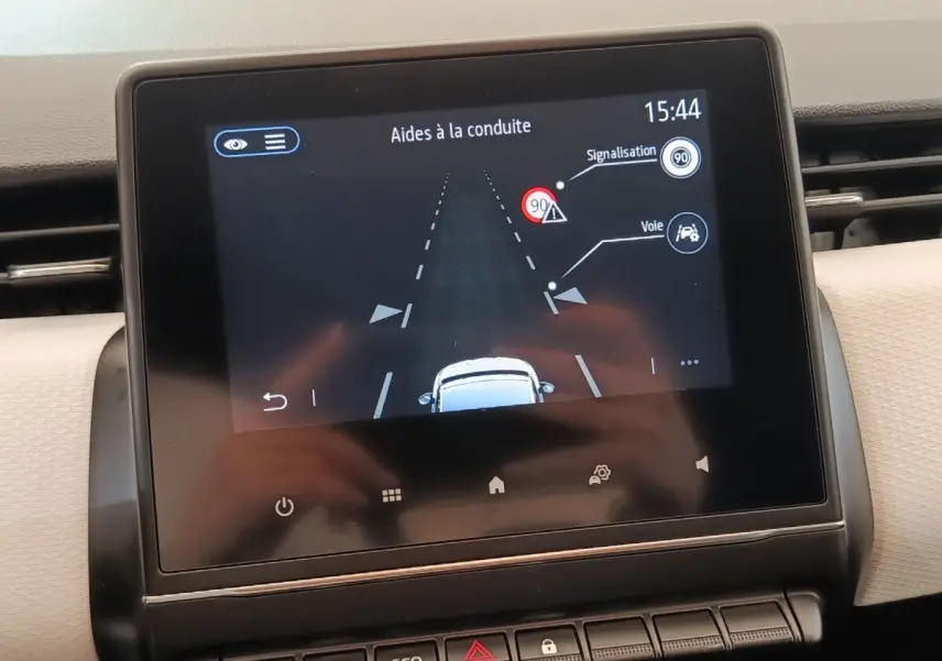 Écran tactile central de la Renault Clio blanc montrant l’aide à la conduite avec alertes de signalisation et voie.