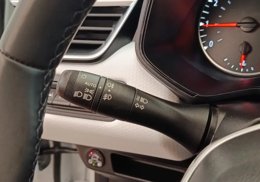 Gros plan sur la commande des phares à gauche du volant d’une Renault Clio blanche, tableau de bord clair visible.