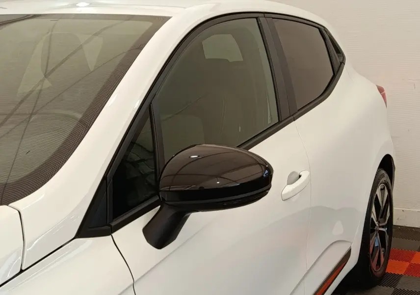 Vue côté gauche avant d'une Renault Clio blanche avec rétroviseur noir brillant et vitres teintées.