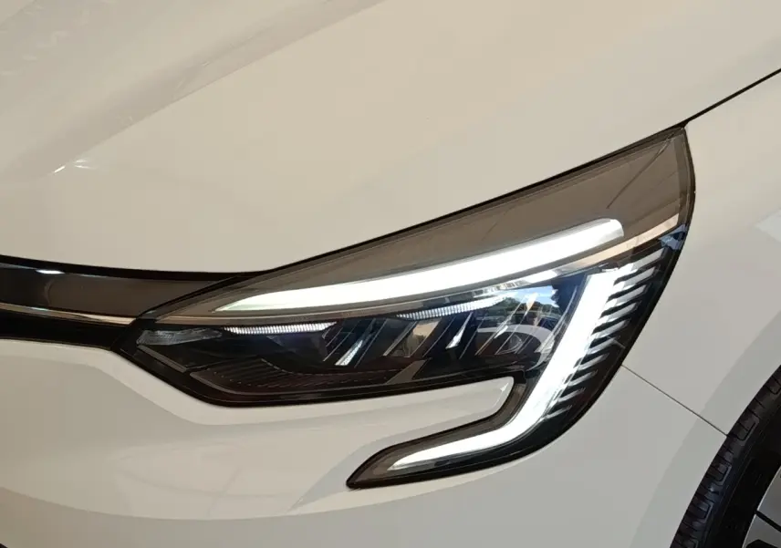 Gros plan sur le phare avant droit allumé d'une Renault Clio Evolution TCe 100 GPL blanche de 2023.