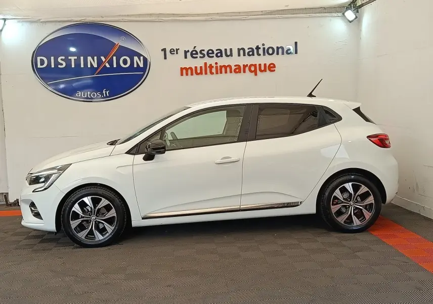 Profil droit d'une Renault Clio Evolution TCe 100 GPL blanche avec jantes alliage et rétroviseurs noirs en intérieur showroom.