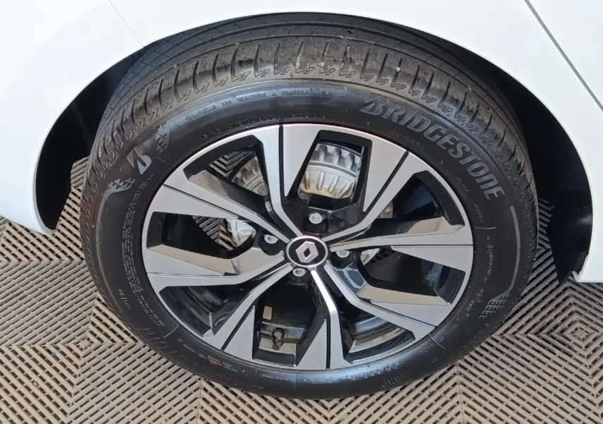Gros plan sur la roue avant droite d’une Renault Clio blanche, jante alliage bicolore avec logo Renault central.