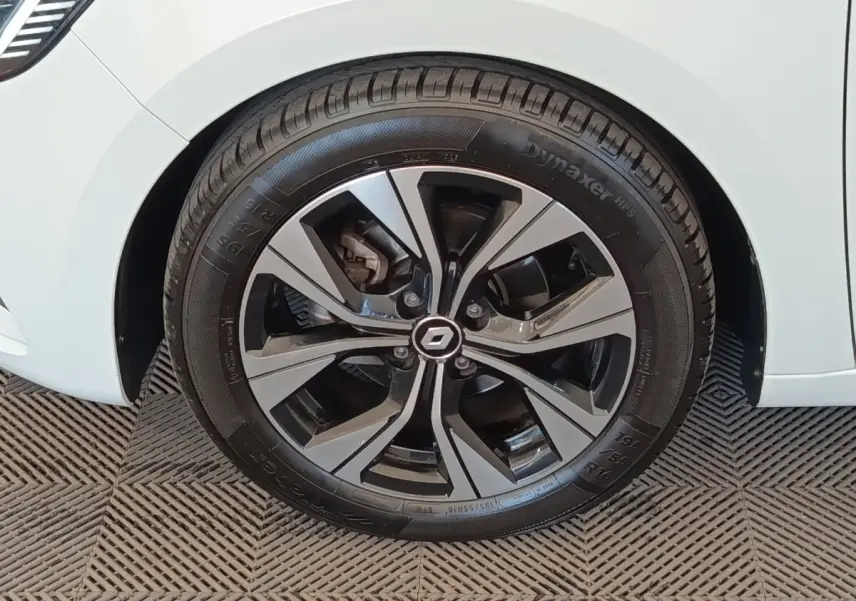 Gros plan sur la roue avant gauche d'une Renault Clio blanche avec jante alliage au design moderne.