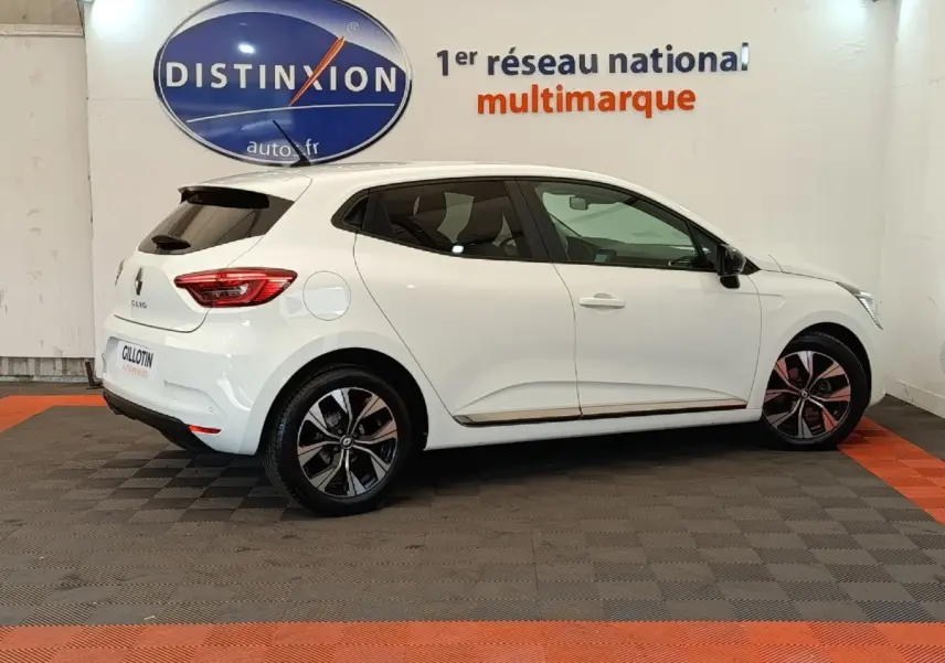 Profil droit d'une Renault Clio blanche Evolution TCe 100 GPL 2023, avec jantes alliage et vitres teintées, en intérieur showroom.