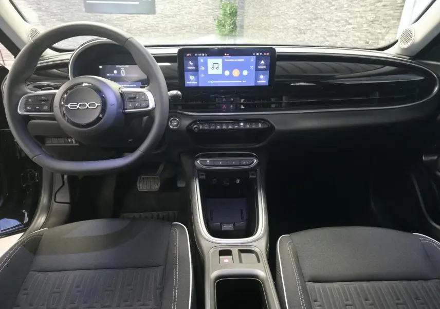 Vue intérieure avant du tableau de bord noir brillant et volant du Fiat 600 Hybrid avec écran tactile central.