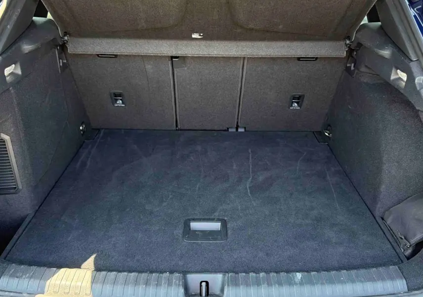 Coffre ouvert vu de l'arrière d'une CUPRA Terramar bleu, espace de chargement avec tapis noir et habillage intérieur sombre.