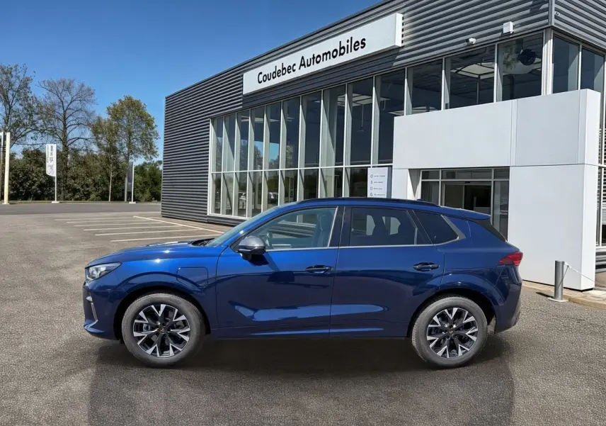 Vue de profil côté gauche d'un CUPRA Terramar bleu métallisé garé devant un bâtiment moderne de concession.