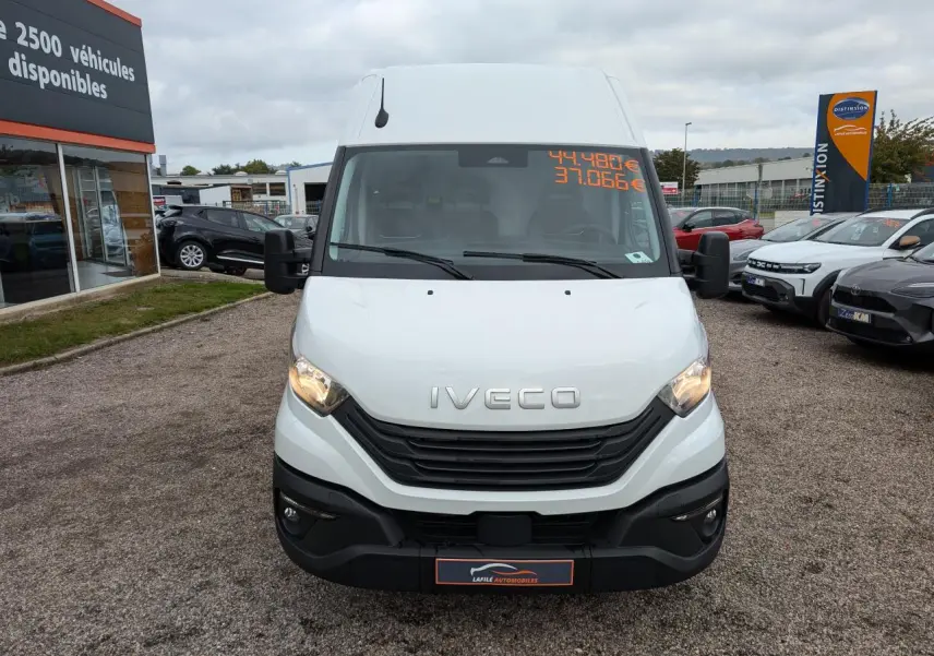 Vue frontale d'un utilitaire Iveco Daily blanc avec calandre noire et phares allumés sur un parking.
