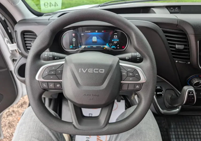 Vue rapprochée du volant IVECO Daily 35S16 avec commandes intégrées et tableau de bord digital en arrière-plan.